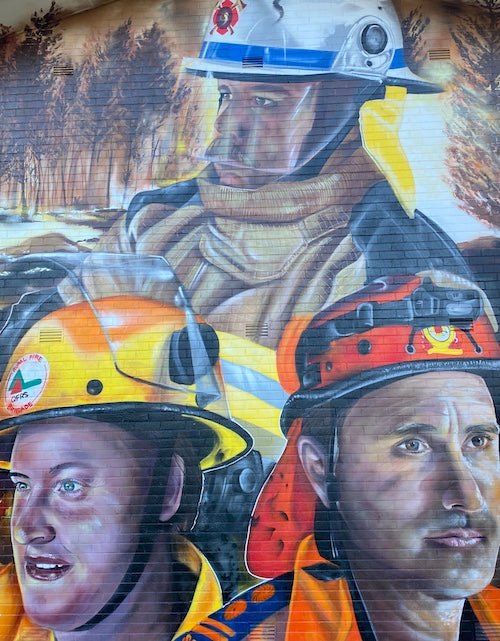three first responder fire fighters in different uniforms with a raging fire in the background commemorating the 2019 bushfires